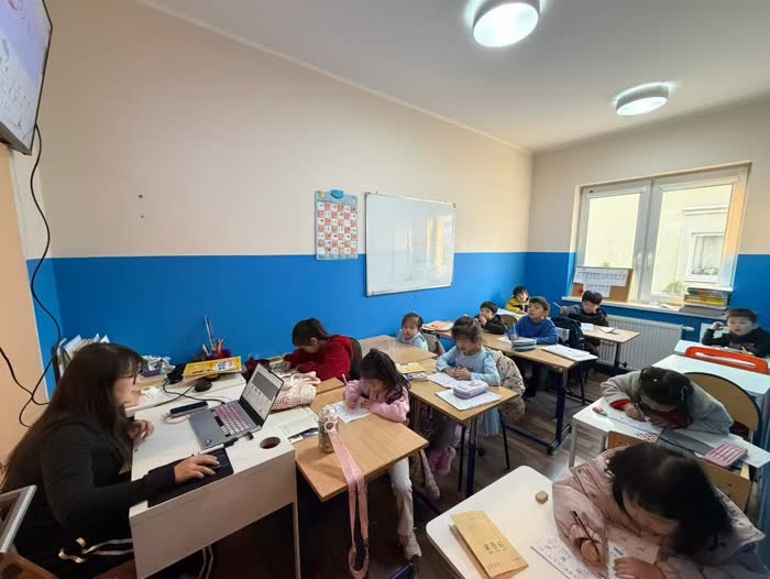 Uczniowie piszą w zeszytach do nauki chińskiego podczas lekcji prowadzonej przez nauczycielkę z laptopem